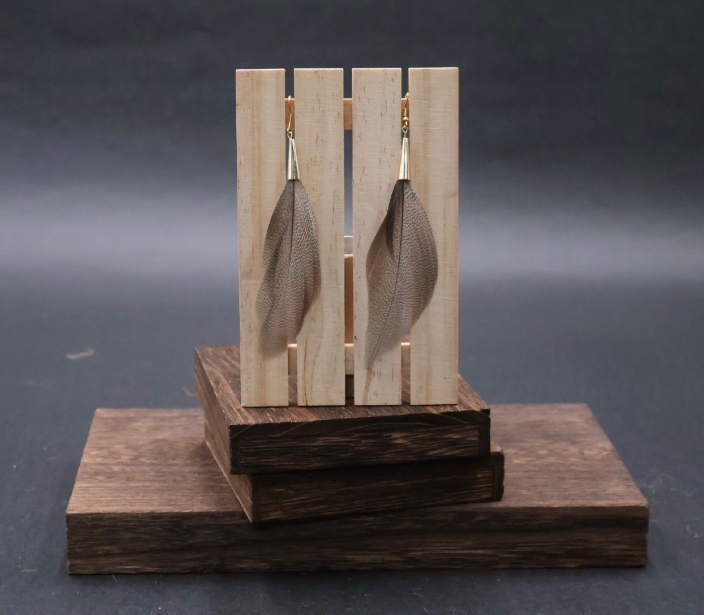 Feather earrings displayed on a light wood stand