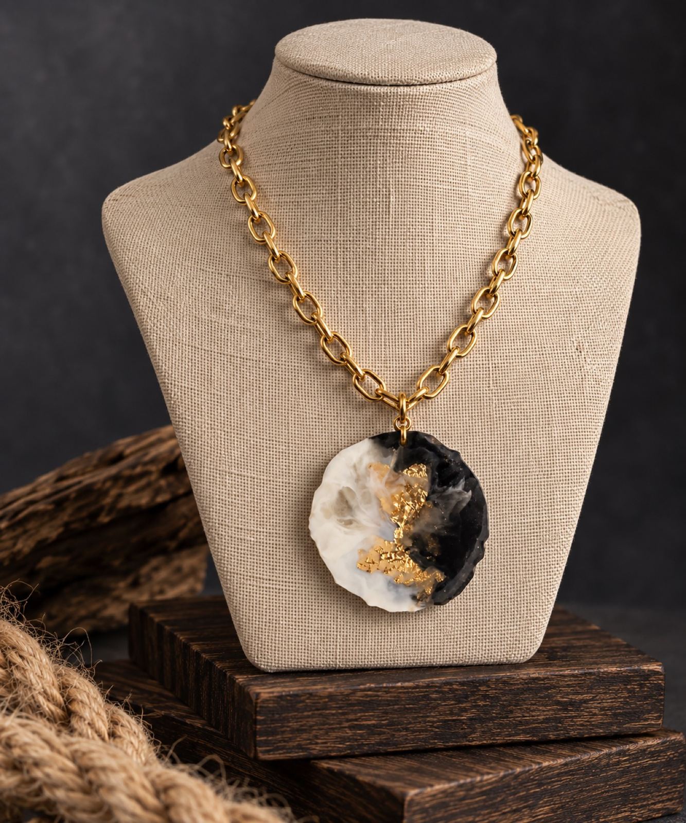 A round resin pendant in black, cream, and gold leaf on a gold chain